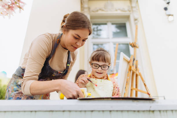 el terapeuta de arte ayuda a pintar a una niña con una discapacidad mental - paintings child house childhood fotografías e imágenes de stock