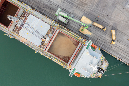 Loading grain into sea cargo vessel in commercial port from trucks. Aerial view.