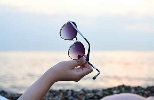 sunglasses in the hands of a woman on the background of the seashore