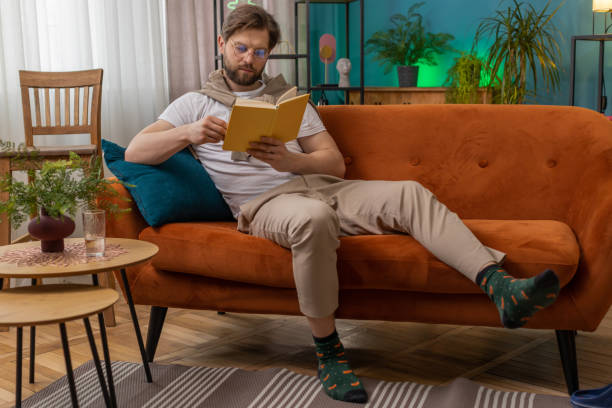 istock Young man relaxing interesting book turning pages smiling enjoying literature taking a rest on sofa 1487976930