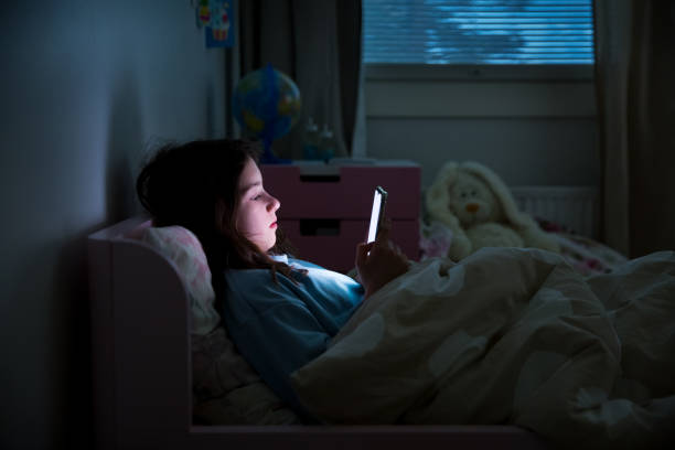 un niño usando un teléfono inteligente acostado en la cama - addiction smart phone internet social networking fotografías e imágenes de stock