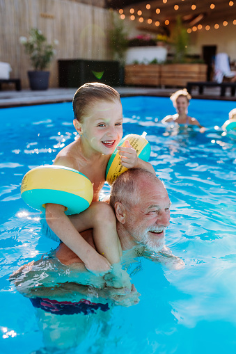 A grandfather with his grandson having fun together when playing in the swimming pool at backyard.