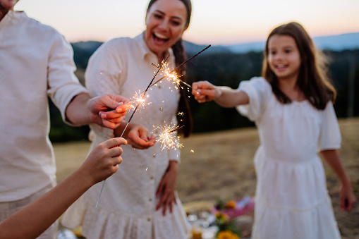 Happy family with children having picnic in the park, clebrating with sparklers.