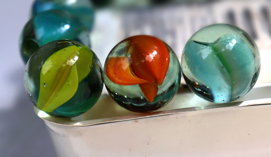 A collection of well used colorful glass marbles from  children's play in the pas in a shallow yellow bowl. .