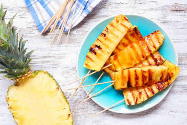 istock Grilled summer pineapple wedges, top down table scene over white wood 1487987739