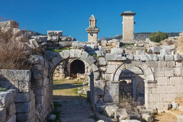 Entrance gate to theatre of Xanthos ancient city - part of Lycian way. Tomb monument of king Kybernis ( Harpy Tomb), Pillar Tomb on background. Popular travel destination in Antalya, Turkey