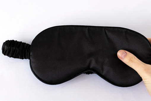 Black silk sleep mask in a woman's hand.