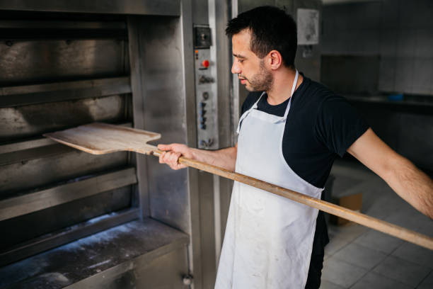 istock Baker taking bread out of oven 1487990525