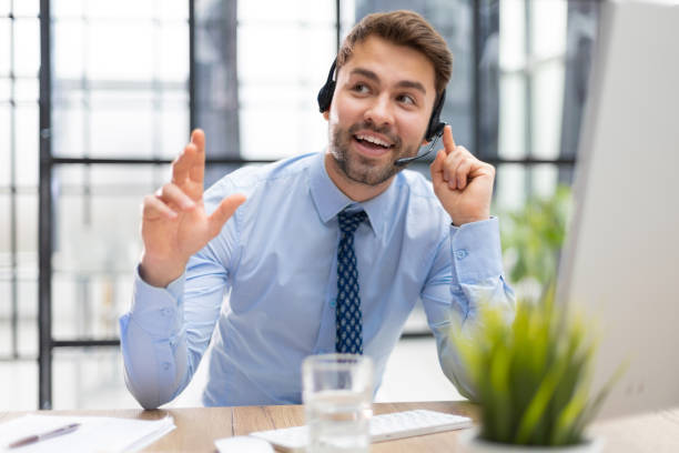 istock Cheerful young support phone male operator in headset, at workplace with collegues on the background while using computer, help service and client consulting call center concept 1487992076