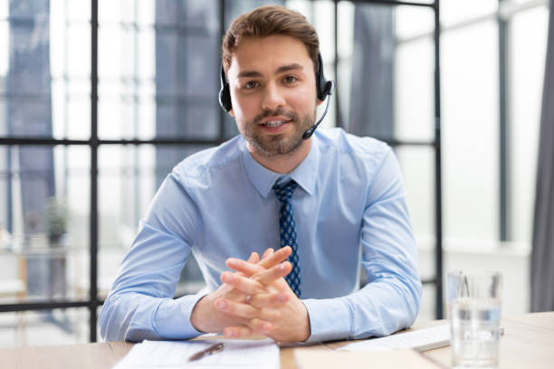 istock Cheerful young support phone male operator in headset, at workplace with collegues on the background while using computer, help service and client consulting call center concept. 1487992092