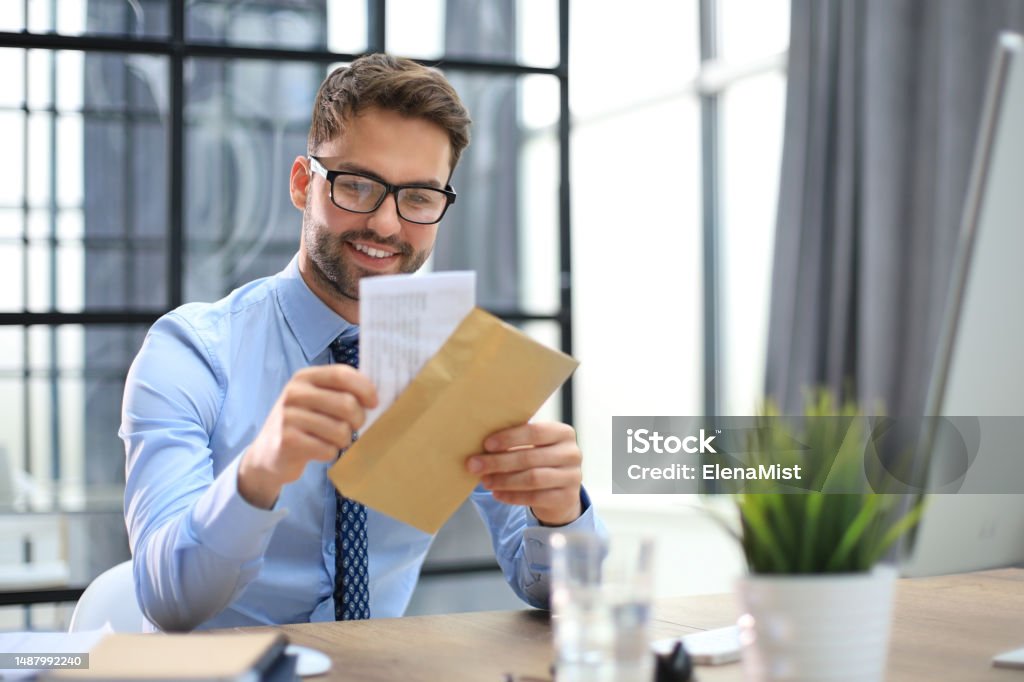 Handsome entrepreneur opening a padded envelope in a desktop at office Handsome entrepreneur opening a padded envelope in a desktop at office. Adults Only Stock Photo