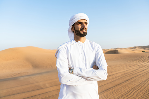 Handsome and successful middle-eastern man wearing traditional emirati arab kandura in the desert - Arabian muslim adult person at the sand dunes in Dubai