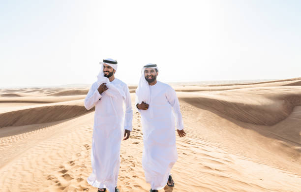 Two middle-eastern emirati men wearing arab kandura bonding in the desert Two middle-eastern men wearing traditional emirati arab kandura bonding in the desert - Arabian muslim friends meeting at the sand dunes in Dubai middle eastern clothes stock pictures, royalty-free photos & images