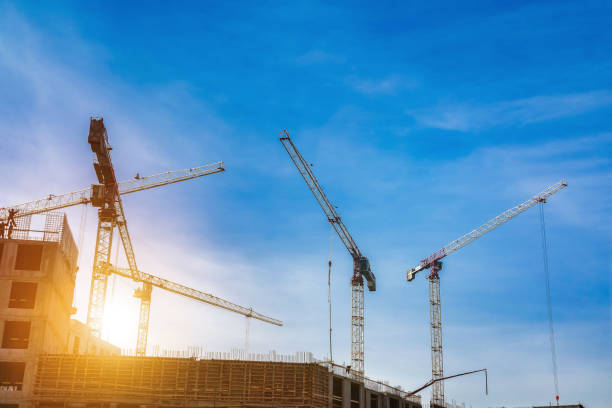 istock Creation site with industry cranes working at cloudy sky sunset backdrop. Bottom view of industrial crane on construction site. Concept of construction and renovation of buildings. Copy ad text space 1487997188