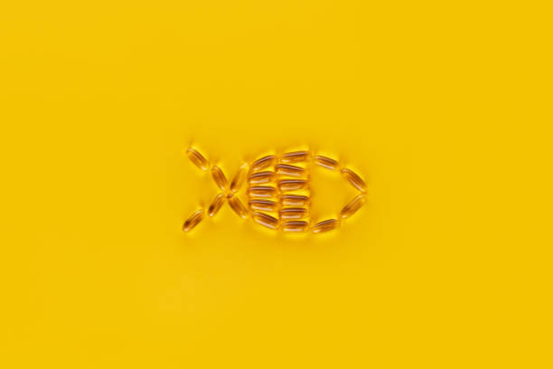 タラ肝油カプセルは黄色の背景に魚の形に配置されています - fish oil vitamin pill cod liver oil nutritional supplement ストックフォトと画像