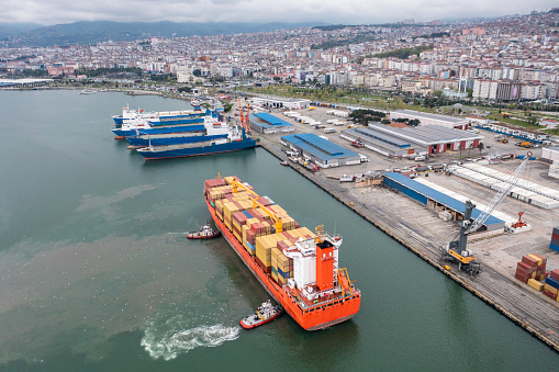 Icel / Turkey - 12 October 2019: Aerial view of cargo container ship approaching port.  Global business logistics import export background and container ship, forklift truck lifting cargo container in shipping yard transport concept.
