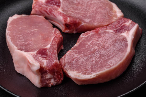 Raw pork on the bone or rib sliced with salt, spices and herbs on a dark concrete background