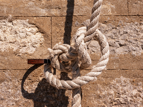 Knot on a thick white rope tied to an oarlock against the background of a stone brick wall front view