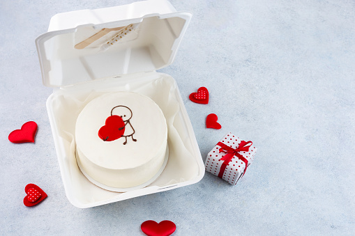 Plastic lunch box with tasty bento cake and gifts for Valentine's Day on white background