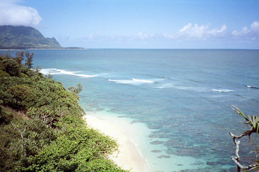 A vintage 1980s film photograph view perched on an ocean bluff overlooking Hanalei Bay, Pali Ke Kua  Kauai, Hawaiian volcanic coastline with hidden beach tucked in the coastline.