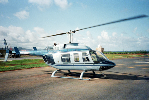 A vintage 1980s film photograph of a helicopter from a Hawaii helicopter tour parked on the runway.