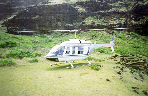 A vintage 1980s film photograph of a touring helicopter parked in the lush landscape of Maui, Hawaii.