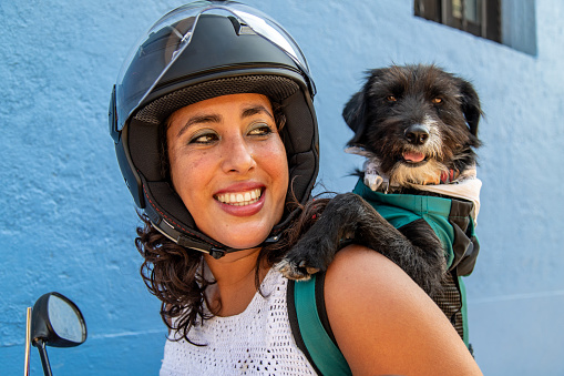 Smiling hispanic woman with motorcycle helmet and dog in  dog carrier