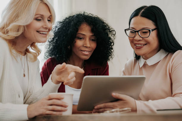 istock Three happy mature women looking at digital tablet while sitting at the desk together 1488018102