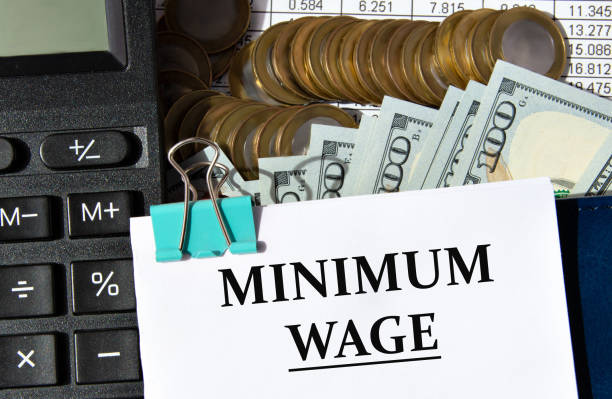 istock MINIMUM WAGE - words on a white sheet against the background of a calculator, banknotes and pennies 1488020113