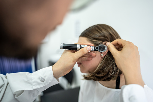 Doctor/otolaryngologist using an otoscope in a patient's ear at medical clinic