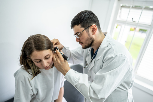 Doctor/otolaryngologist using an otoscope in a patient's ear at medical clinic