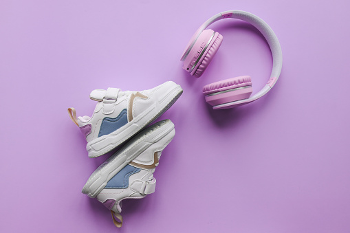 White children's sneakers and headphones on a pink background with copy space. Banner.