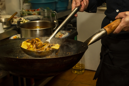 Hands of an Asian chef stir frying a wok beef with bamboo in the kitchen of a European Chinese restaurant