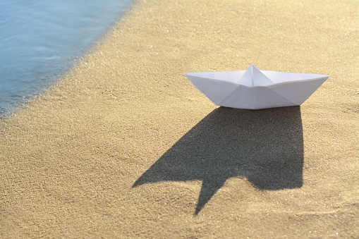 Beautiful white paper boat on sand near sea, space for text