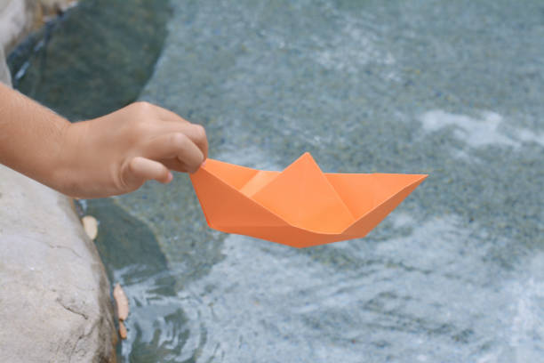 istock Kid launching small orange paper boat on water outdoors, closeup 1488043949