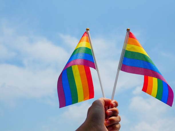 istock Hands waving LGBTQ rainbow flag against blue sky 1488057831