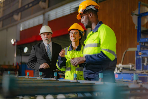 Senior boss manager inspecting with staff engineers woman and African man.Team checking construction structure of factory building. warehouse with steel roof structure and machine installation. gerente jefe superior inspeccionando con ingenieros de personal mujer y hombre africano. equipo de comprobación de la estructura de construcción del edificio de la fábrica. almacén con estructura de techo de acero e instalación de máquina.