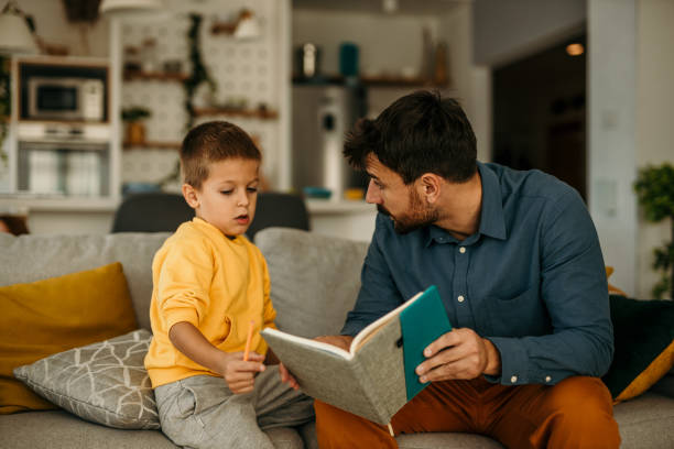 istock Father holding a notebook and educating his son while both spending time in the living room. 1488069903