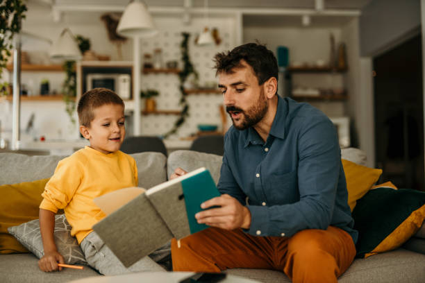 istock Father holding a notebook and educating his son while both spending time in the living room. 1488069904