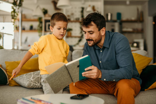 istock Father holding a notebook and educating his son while both spending time in the living room. 1488069905