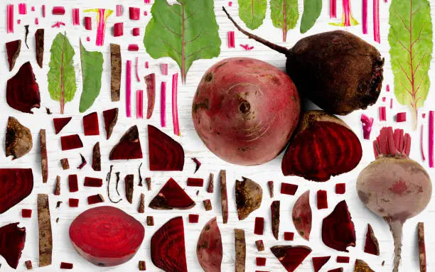 Abstract background made of Red Beet vegetable pieces, slices and leaves on wooden background.