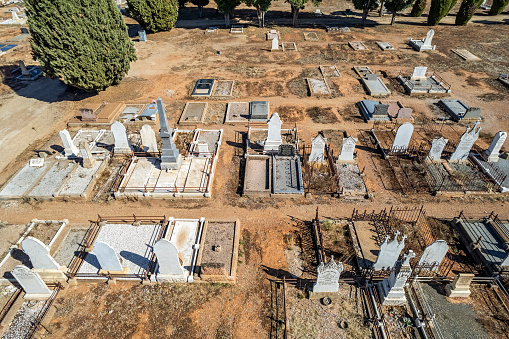Burra, Australia - April 14, 2023: Aerial wide view, looking down on neat, orderly graves and headstones in the historic Burra cemetery: marked graves, unmarked graves, simple and elaborate headstones and borders; barren earth, no green lawn or turf.