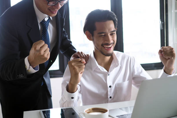 マネージャーとスタッフは、コンピューターを見ながら陽気に見えました。勝者のコンセプト - cheering business people group of people ストックフォトと画像