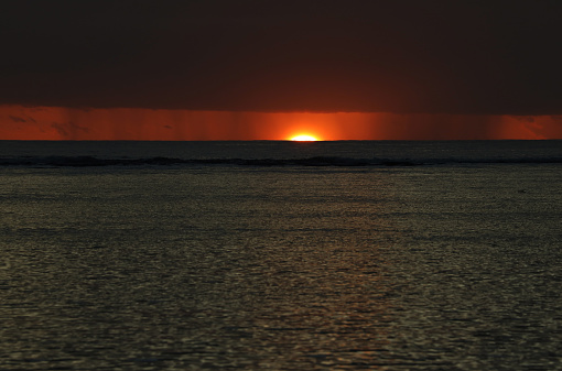 Albion, Mauritius - May 05, 2023: Vibrant colors and rain during sunset at the Indian Ocean close the public beach of Albion in the West of Mauritius during a cloudy day. Some clouds make the scenery more spectaculor.