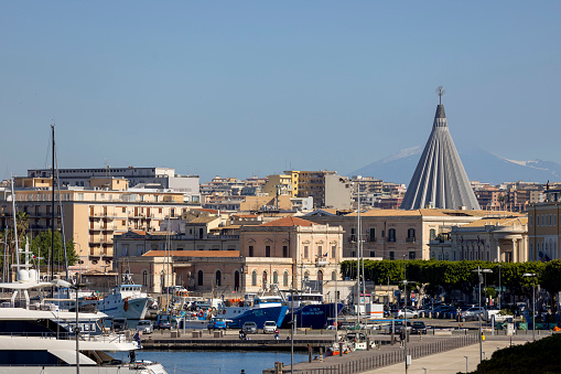 Syracuse, Sicily, Italy - April 29, 2023: View from Foro V. Emanuele II of port and city with Basilica of the Madonna delle Lacrime. Mount Etna in the distance