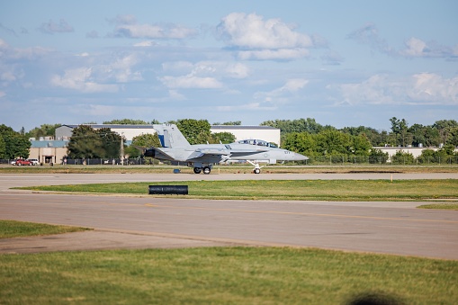 OshKosh, United States – July 29, 2022: An F-18 variant airplane on a runway at Wittman Regional Airport, with the sky and trees visible in the background