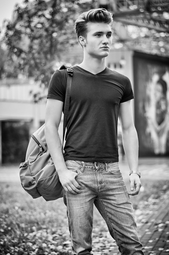 Attractive young man standing in city environment, with rucksack on one shoulder