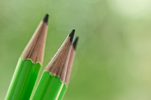 three sharp green wooden pencil on blur nature background with bokeh