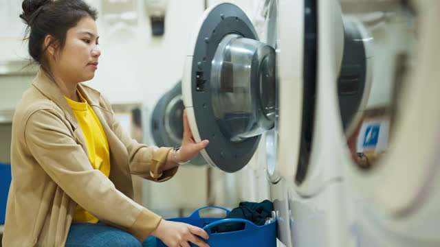 Asian woman traveller taking off clean cloth from laundry machine after finish,Beautiful woman is washing clothes in an automatic  laundromat