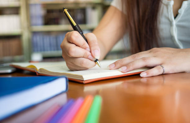 istock Female students writing books inside the library. Do homework and report to teachers 1488097371